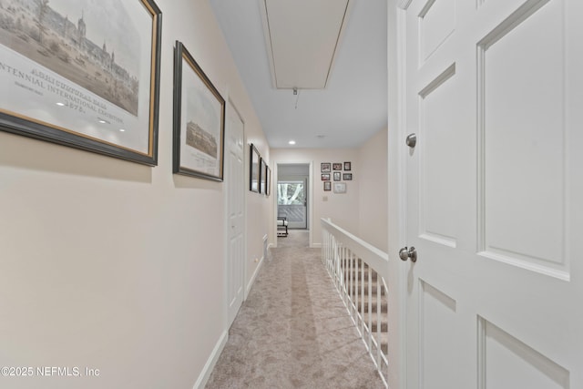 hall with light carpet, attic access, and baseboards