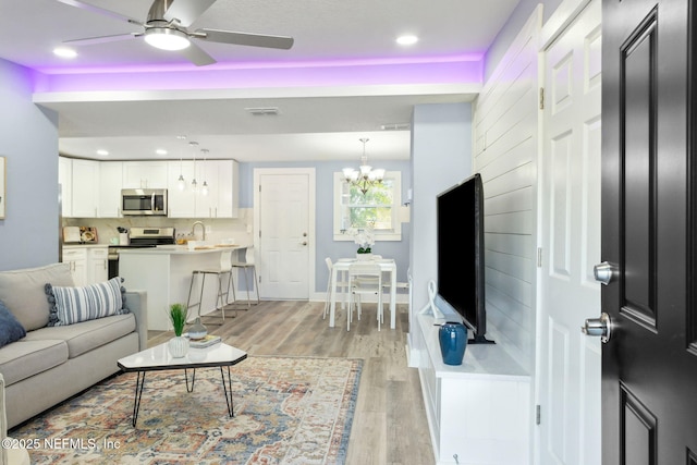 living area with light wood-style flooring, recessed lighting, ceiling fan with notable chandelier, visible vents, and baseboards