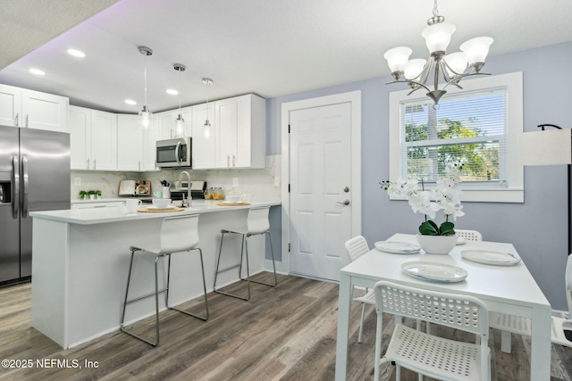 kitchen featuring stainless steel appliances, tasteful backsplash, white cabinets, wood finished floors, and a peninsula