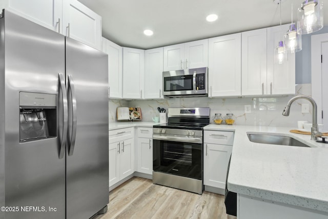 kitchen featuring light stone counters, a sink, white cabinets, appliances with stainless steel finishes, and light wood-type flooring