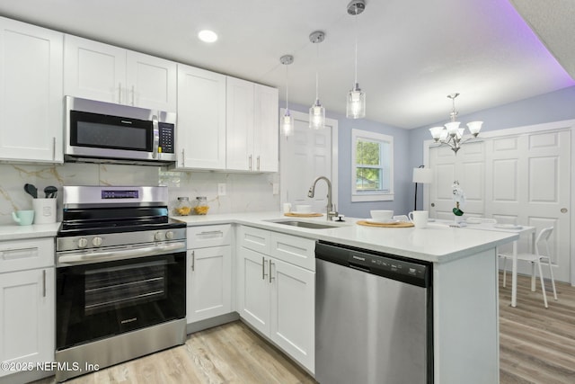 kitchen featuring stainless steel appliances, light countertops, white cabinetry, a sink, and a peninsula