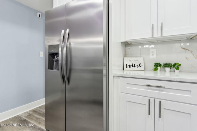 kitchen featuring light stone counters, white cabinetry, wood finished floors, stainless steel fridge, and baseboards