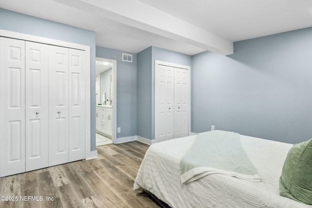 bedroom featuring multiple closets, visible vents, connected bathroom, wood finished floors, and baseboards