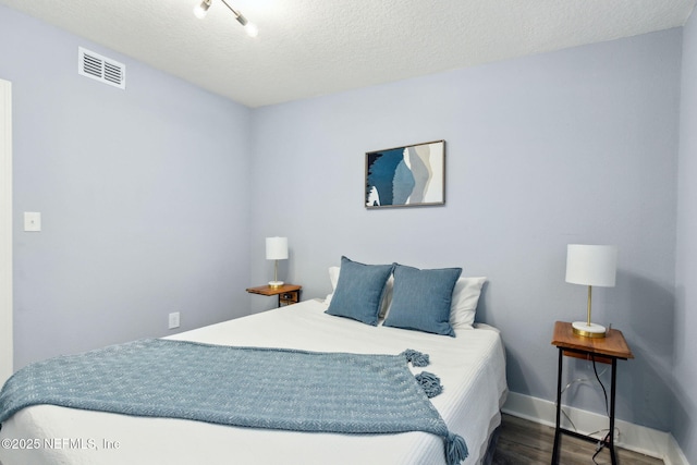 bedroom featuring baseboards, a textured ceiling, visible vents, and wood finished floors