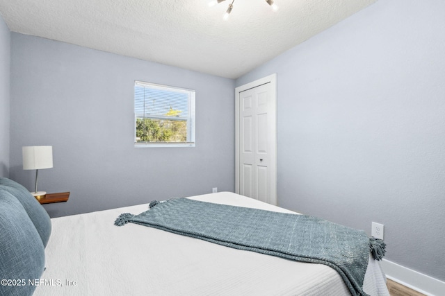 bedroom with a textured ceiling, a closet, wood finished floors, and baseboards