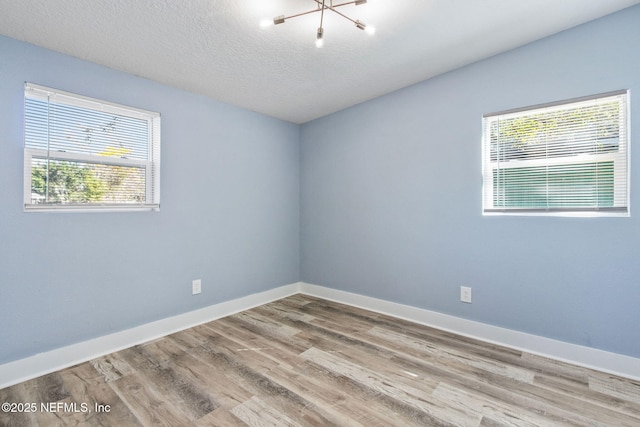 unfurnished room with a notable chandelier, a textured ceiling, baseboards, and wood finished floors