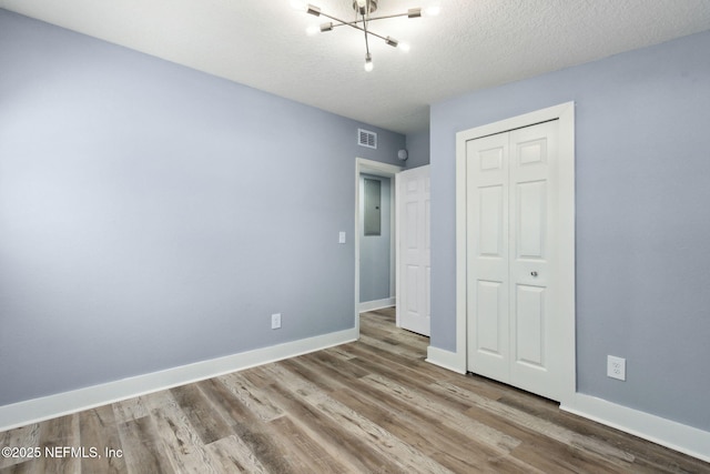 unfurnished bedroom featuring a closet, visible vents, a textured ceiling, wood finished floors, and baseboards