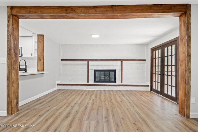 unfurnished living room featuring brick wall, a sink, wood finished floors, baseboards, and french doors