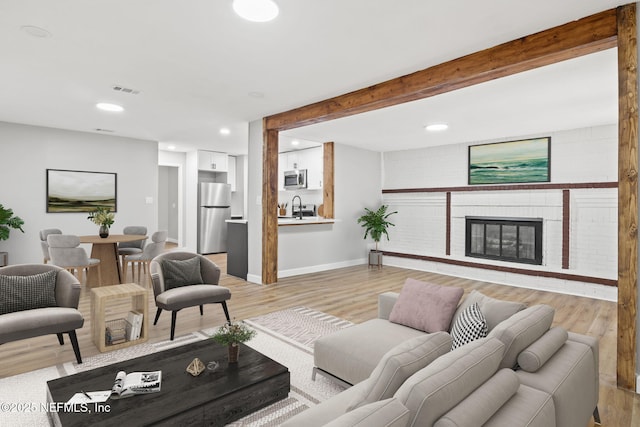 living room featuring light wood finished floors, baseboards, beamed ceiling, a fireplace, and recessed lighting