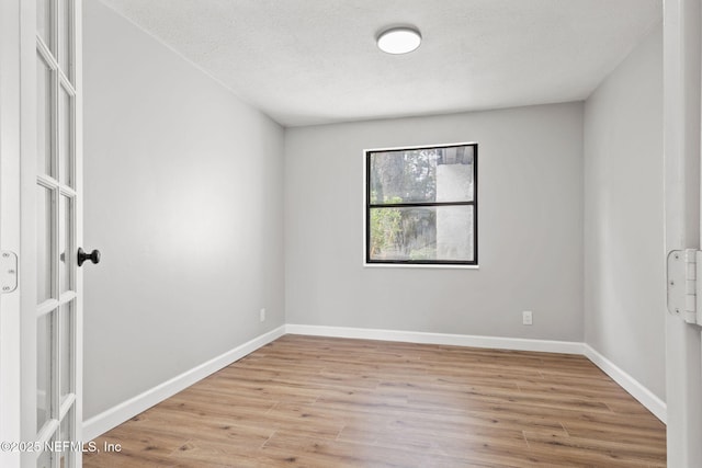 spare room with a textured ceiling, light wood-type flooring, and baseboards