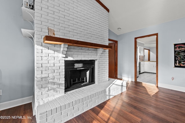 unfurnished living room featuring lofted ceiling, a brick fireplace, baseboards, and wood finished floors