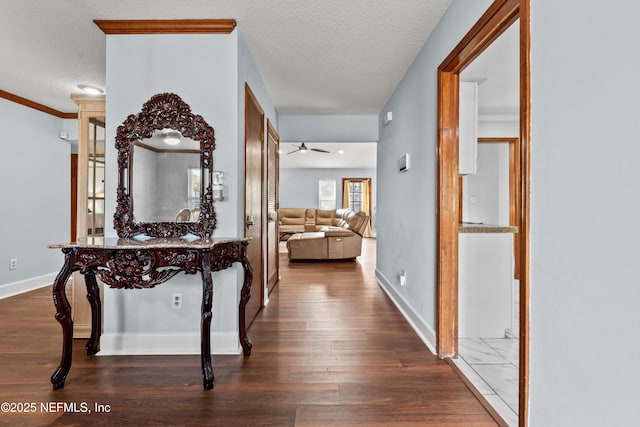 hallway featuring a textured ceiling, ornamental molding, dark wood-style flooring, and baseboards