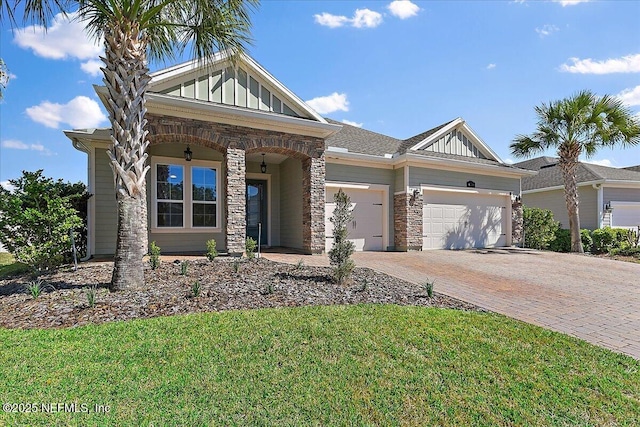 craftsman-style home with a garage, stone siding, decorative driveway, a front lawn, and board and batten siding