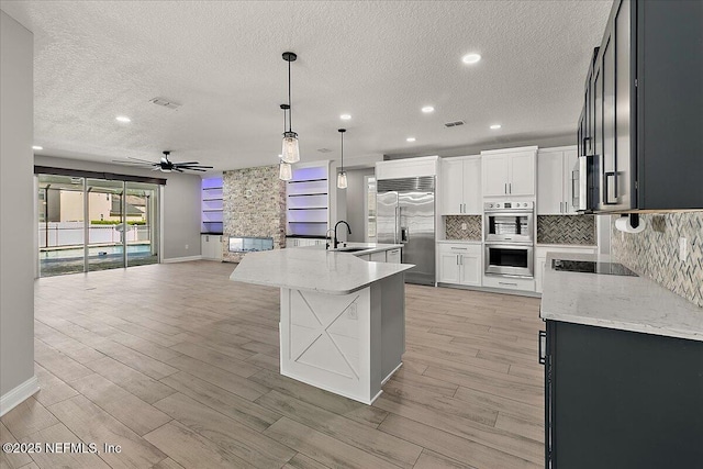 kitchen featuring backsplash, appliances with stainless steel finishes, a ceiling fan, open floor plan, and a sink