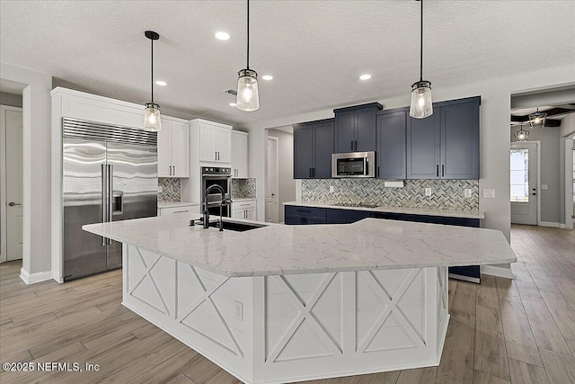 kitchen featuring decorative backsplash, a large island, appliances with stainless steel finishes, light wood-style floors, and a sink