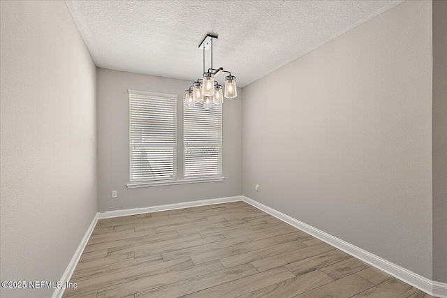 empty room featuring light wood finished floors, baseboards, a chandelier, and a textured ceiling