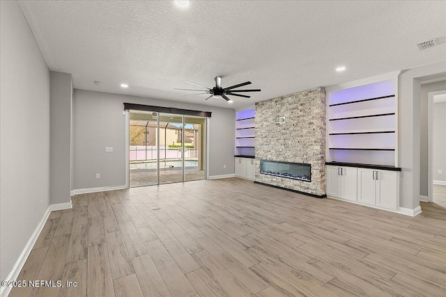 unfurnished living room featuring light wood-style flooring, visible vents, a textured ceiling, and a stone fireplace