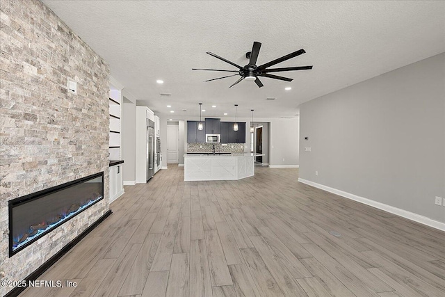 unfurnished living room with a textured ceiling, a fireplace, light wood-style flooring, and a ceiling fan