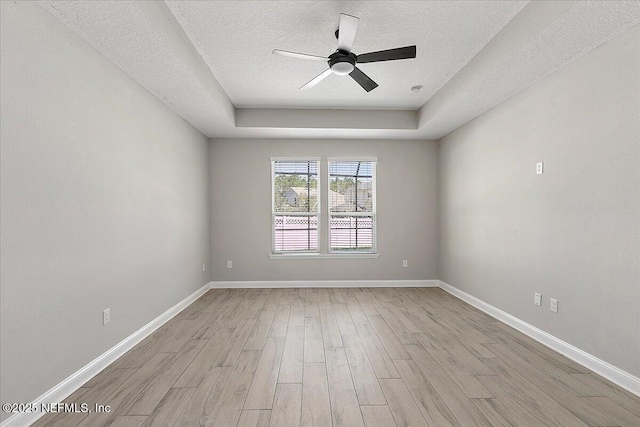 empty room with light wood-style floors, a tray ceiling, a textured ceiling, and baseboards