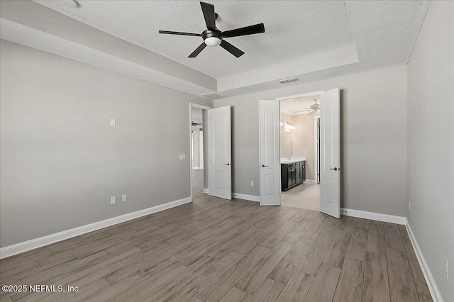 unfurnished bedroom with a tray ceiling, wood finished floors, visible vents, and baseboards