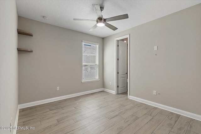 spare room featuring a ceiling fan, light wood-type flooring, a textured ceiling, and baseboards