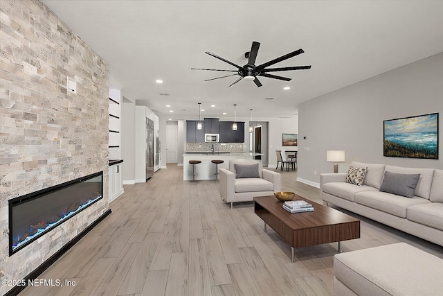 living area featuring light wood finished floors, baseboards, a ceiling fan, a fireplace, and recessed lighting