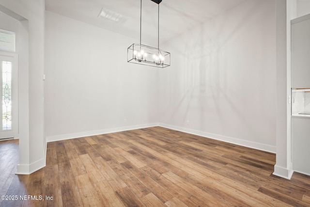 unfurnished dining area featuring wood-type flooring, visible vents, baseboards, and a notable chandelier