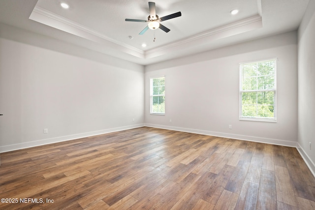 spare room featuring ornamental molding, a tray ceiling, wood-type flooring, and baseboards