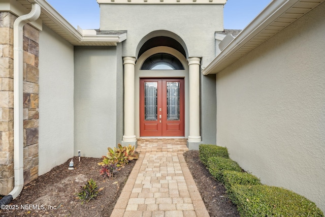 view of exterior entry featuring stone siding, french doors, and stucco siding