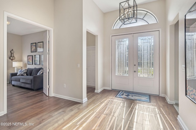 foyer entrance featuring a notable chandelier, french doors, wood finished floors, and baseboards