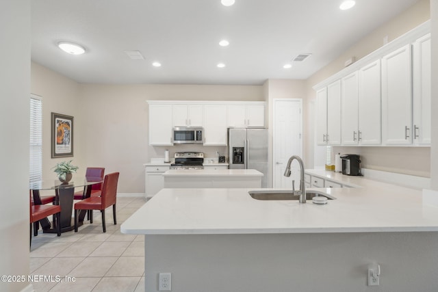 kitchen featuring light tile patterned flooring, stainless steel appliances, a peninsula, a sink, and visible vents