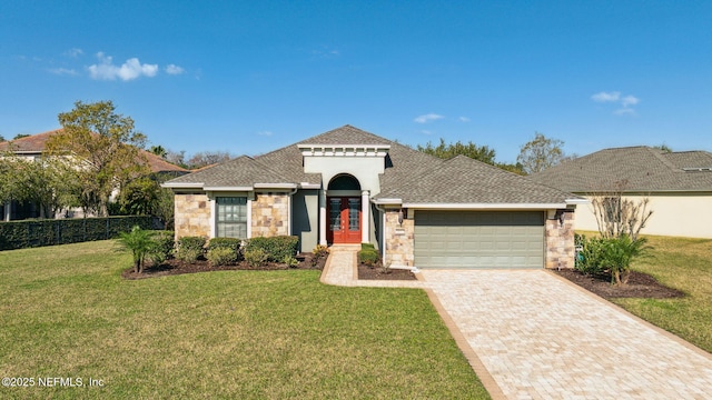 mediterranean / spanish house with a garage, stone siding, decorative driveway, roof with shingles, and a front yard