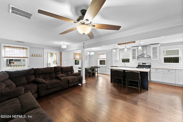 living room featuring ornamental molding, ceiling fan with notable chandelier, visible vents, and wood finished floors