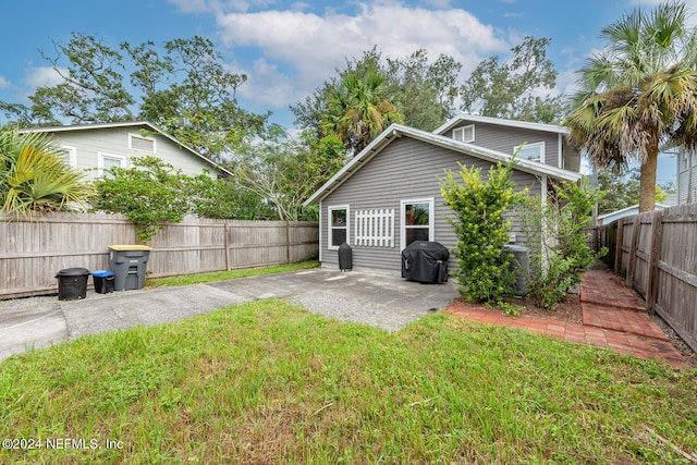 rear view of house with a fenced backyard, a patio, driveway, and a lawn