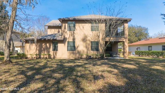 rear view of property featuring a lawn, a patio area, and a balcony