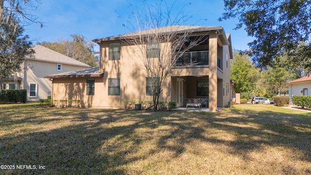 rear view of property featuring a lawn, a balcony, and a patio