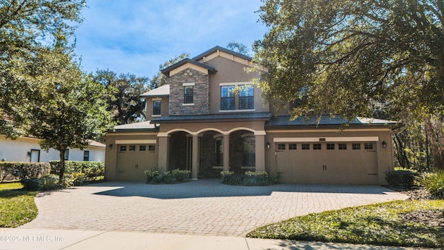 view of front of house featuring a garage, stone siding, decorative driveway, and stucco siding