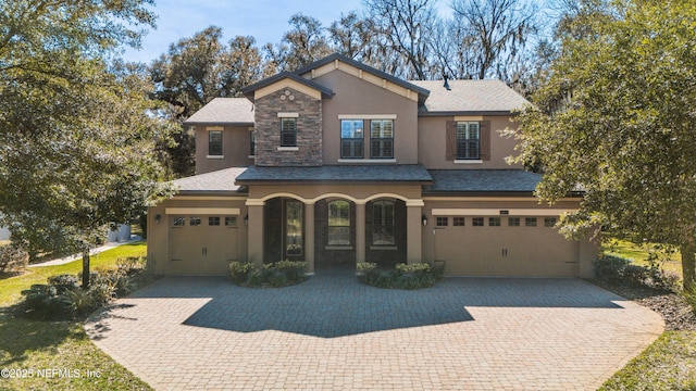 traditional home with a garage, stone siding, decorative driveway, and stucco siding