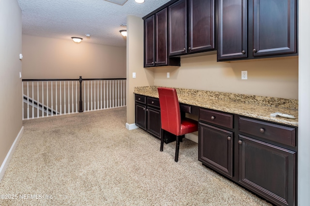 office space with a textured ceiling, built in desk, light carpet, and baseboards