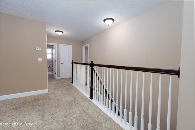 hallway featuring carpet floors, baseboards, and a textured ceiling