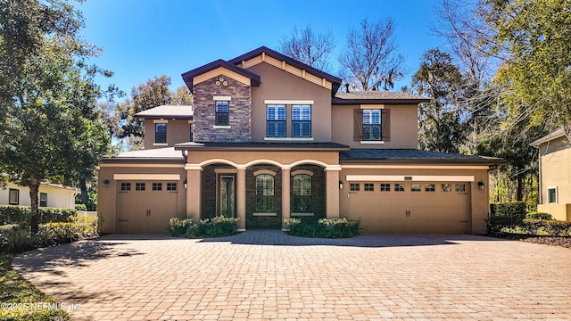 view of front of house with a garage, stone siding, decorative driveway, and stucco siding