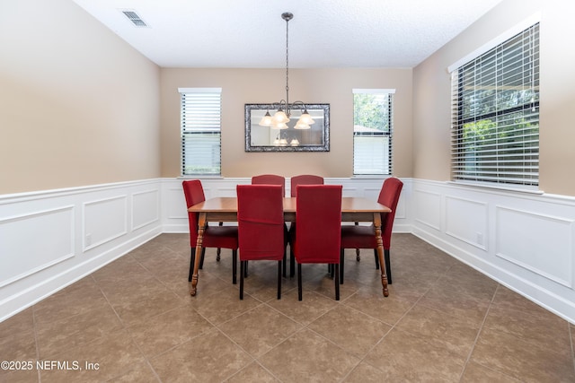 tiled dining area featuring a chandelier, a textured ceiling, visible vents, and a decorative wall