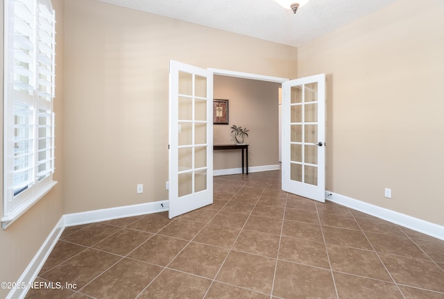 unfurnished room with tile patterned floors, baseboards, a textured ceiling, and french doors