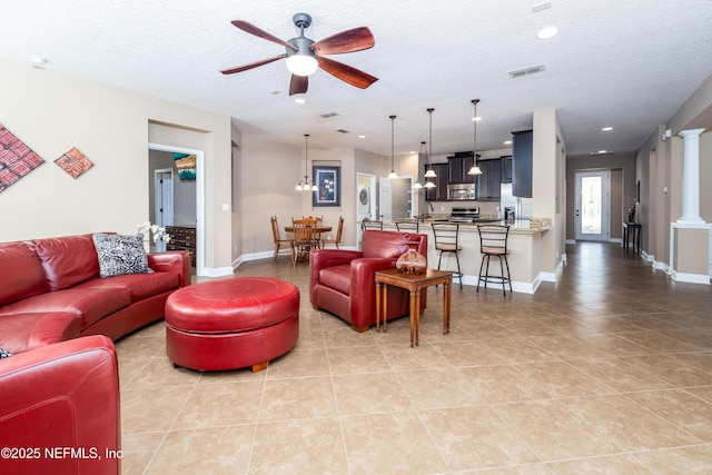 living area featuring decorative columns, visible vents, ceiling fan, and a textured ceiling