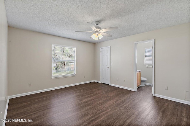 unfurnished bedroom featuring a textured ceiling, dark wood-style flooring, ensuite bath, and baseboards