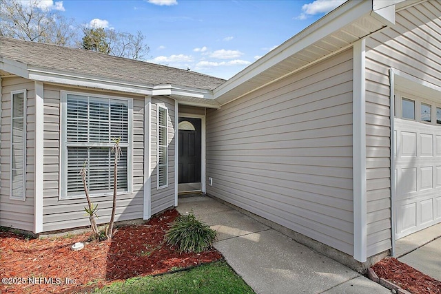 view of exterior entry featuring a garage and a shingled roof