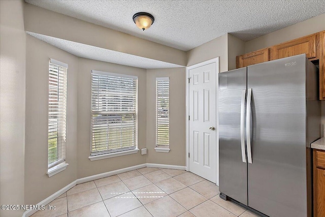 kitchen featuring light tile patterned floors, a textured ceiling, freestanding refrigerator, and brown cabinets