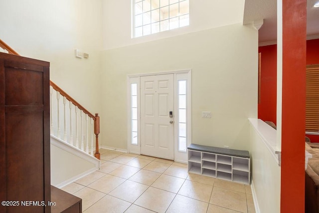 tiled foyer entrance with ornamental molding, a high ceiling, baseboards, and stairs