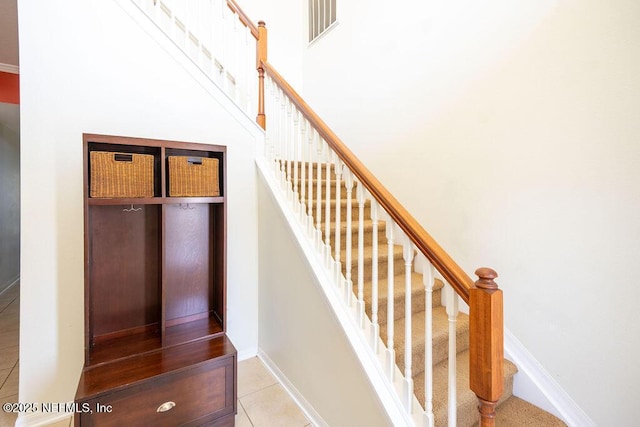 staircase featuring a towering ceiling, baseboards, visible vents, and tile patterned flooring