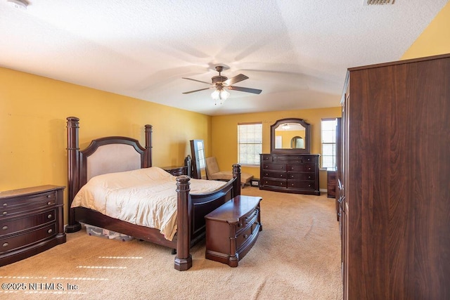 bedroom featuring a ceiling fan, visible vents, light carpet, and a textured ceiling